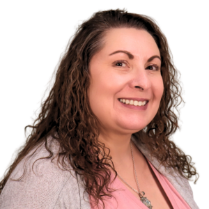 Light-skinned woman with curly medium-brown hair, wearing a silver necklace, pink v-neck shirt, and soft-gray cardigan.