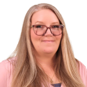 Light-skinned woman with straight blonde hair, wearing glasses, a gold necklace, and a pink v-neck shirt.