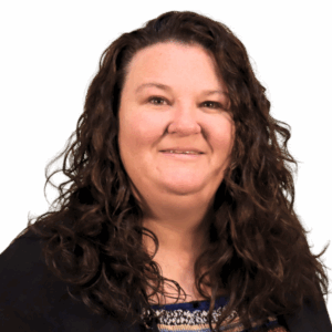 Janet T Light-skinned female with long curly brown hair, wearing a black jacket and blue patterned shirt.